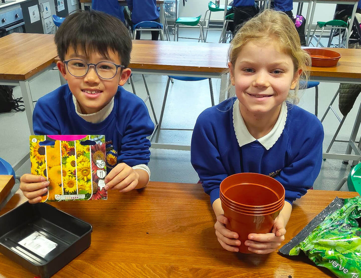 A photo of 2 children holding a plant pot and some seeds to get ready to plant